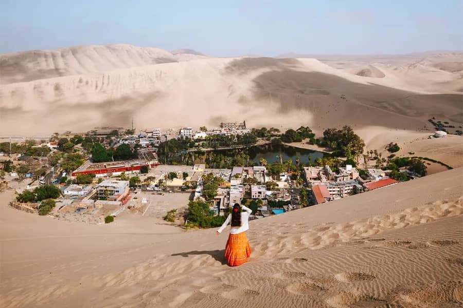 Vista de la Huacachina desde las dunas del desierto con una viajera observando el oasis