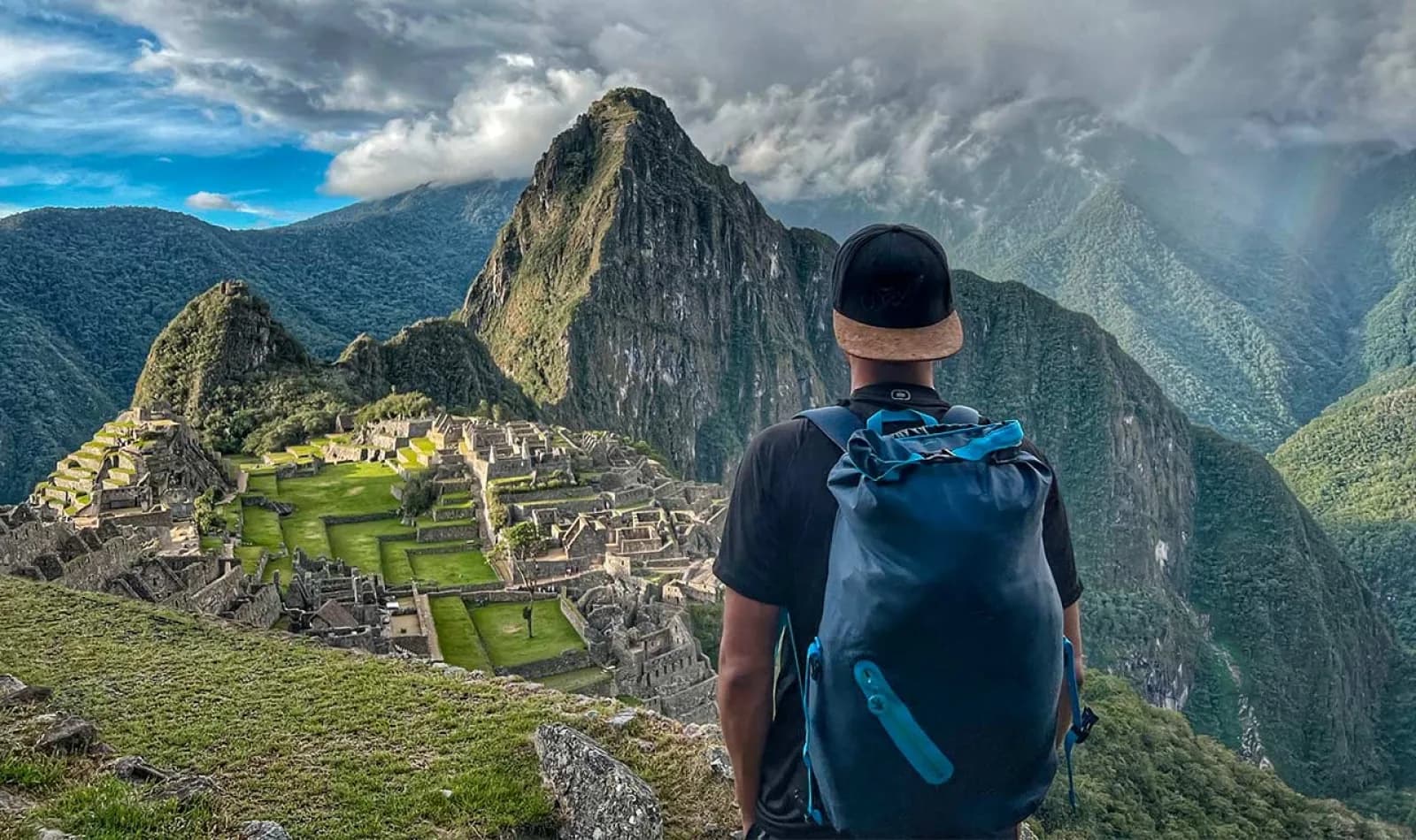 Viajero observando Machu Picchu, con una mochila azul grande. 