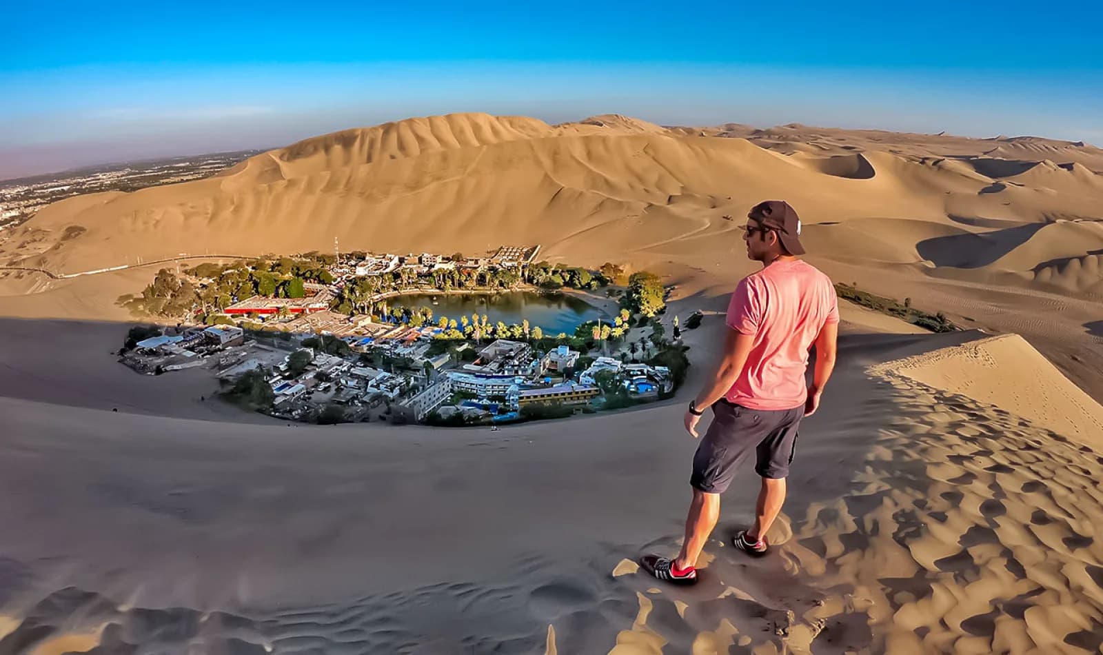 Viajero observando el Oasis de la Huacachina en un día soleado.