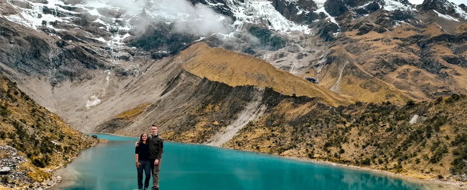 Pareja de viajeros frente a la laguna Humantay y las montañas nevadas de Cusco