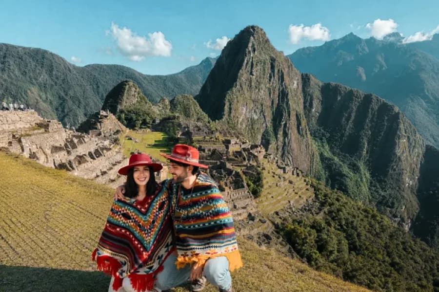 Pareja de viajeros con ponchos andinos frente a la ciudadela de Machu Picchu