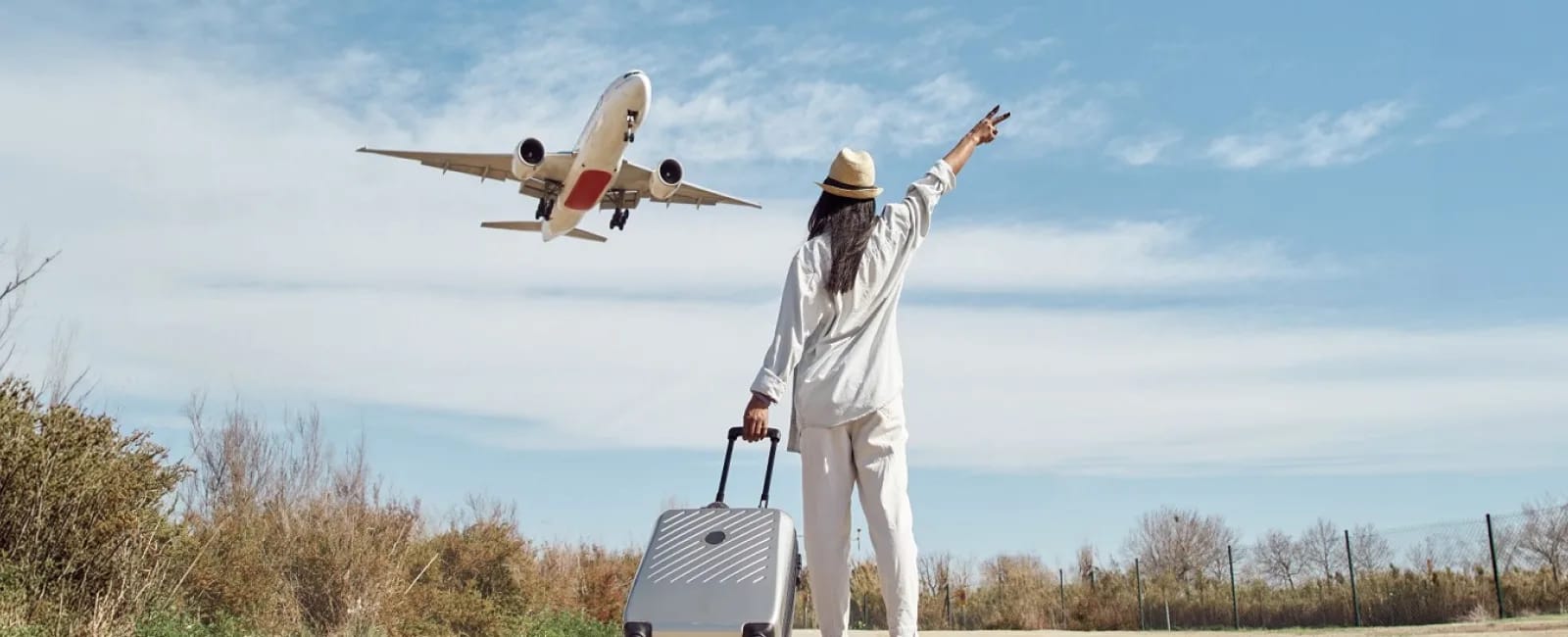 Viajera con maleta observando un avión que despega