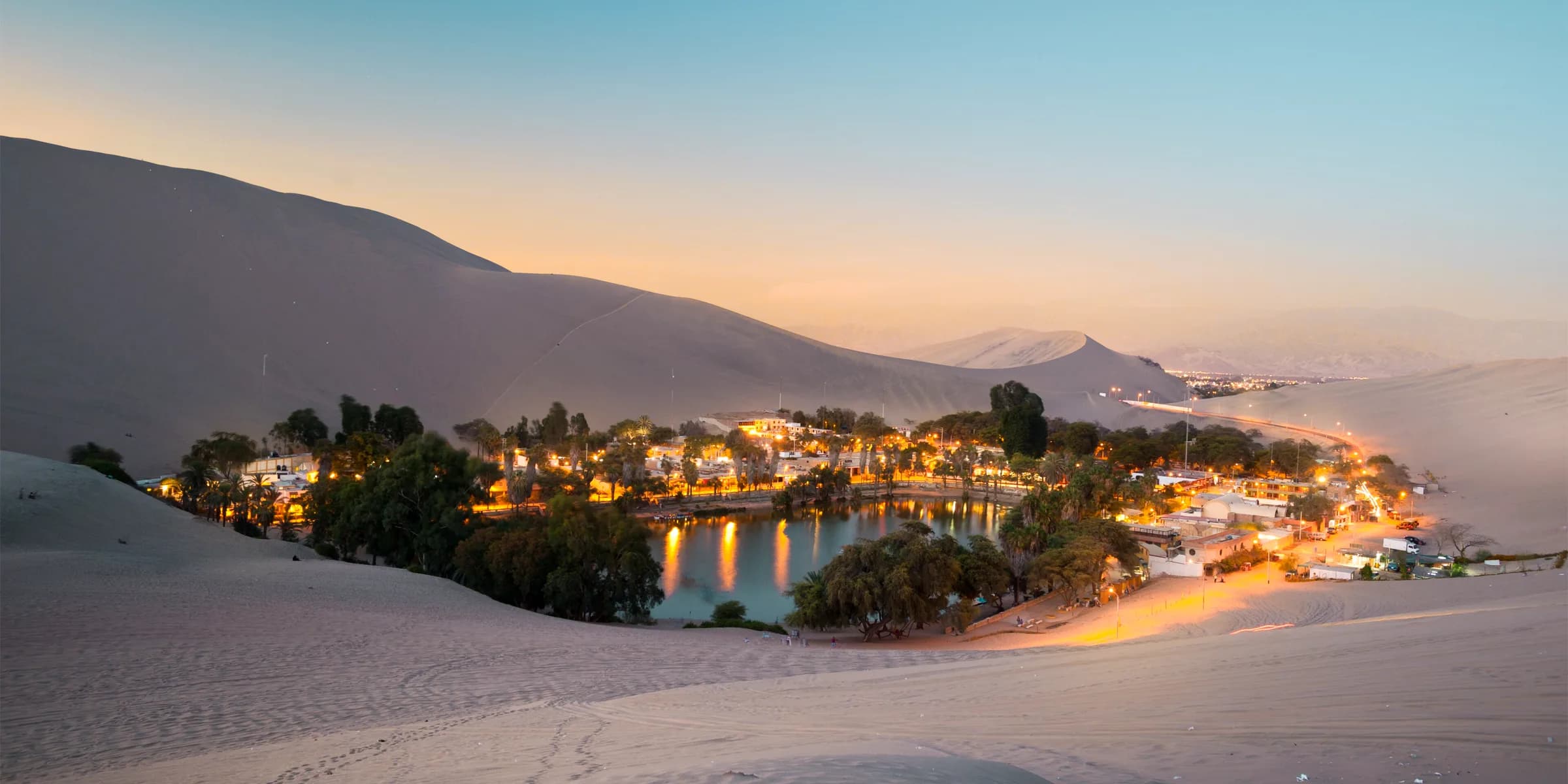 Vista panorámica del oasis de Huacachina iluminado al atardecer entre las dunas de Ica